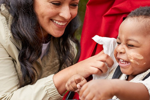 A smiling mother reaches to wipe a laughing baby's messy face with a Huggies Simply Clean fragrance-free Wipe